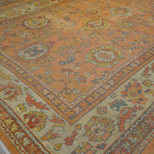 Faded orange traditional rug with tan floral borders and blue accents on rustic wood flooring.