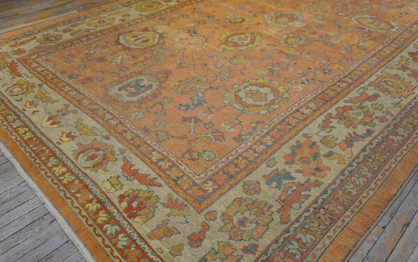 Faded orange traditional rug with tan floral borders and blue accents on rustic wood flooring.