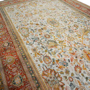 Low-pile rug with a cream field, orange and yellow faded floral patterns, and a thick red border.