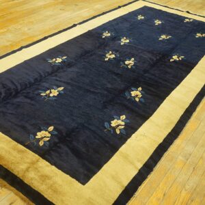 Navy blue rug featuring scattered cream flowers and a wide golden border rests on yellow wood planks.