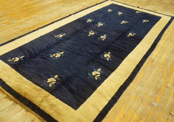 Navy blue rug featuring scattered cream flowers and a wide golden border rests on yellow wood planks.