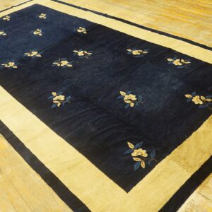 Indigo rug with scattered pale floral motifs and a wide gold border rests on wood flooring.
