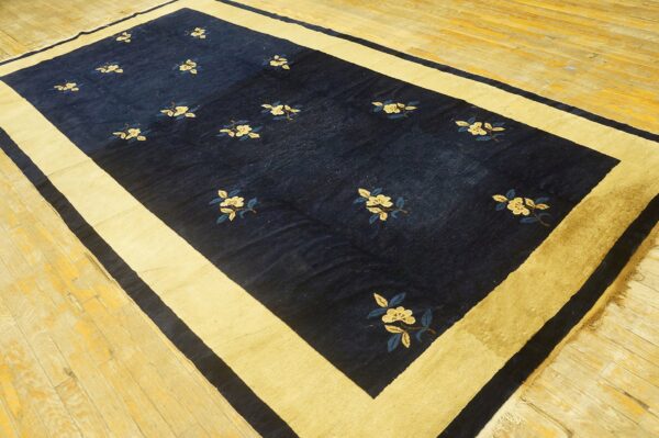 Indigo rug with scattered pale floral motifs and a wide gold border rests on wood flooring.