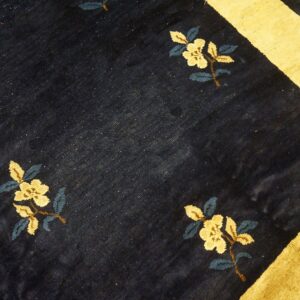 A navy blue rug with scattered yellow floral motifs and a wide gold border stripe rests on wood floorboards.