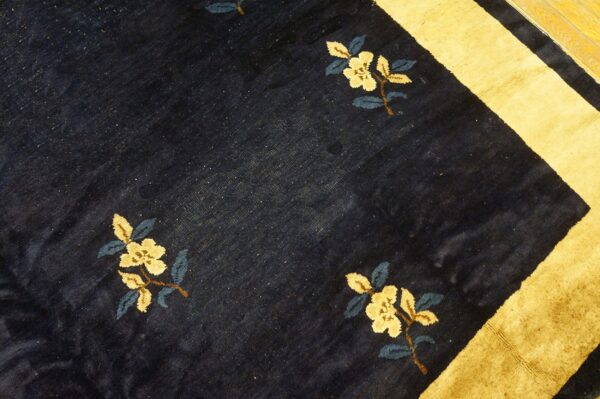 A navy blue rug with scattered yellow floral motifs and a wide gold border stripe rests on wood floorboards.