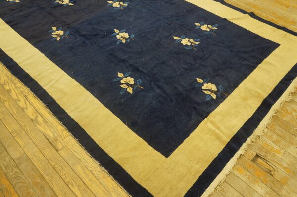 Large navy and gold rug with floral motifs rests on worn yellow wooden planks.