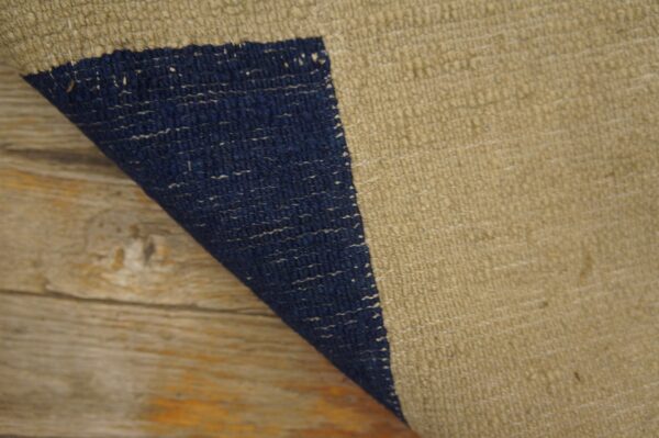 A flatwoven tan rug with a navy blue stripe is partially curled over rustic wood flooring.