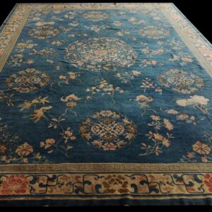 Large blue rug featuring scattered floral and medallion motifs in pink and beige, framed by a wide border.