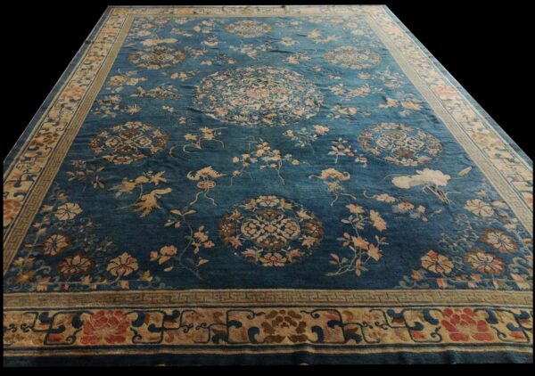 Large blue rug featuring scattered floral and medallion motifs in pink and beige, framed by a wide border.
