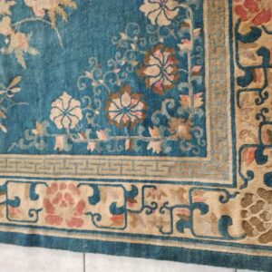 Teal rug with tan and pink floral motifs, featuring multi-layered borders on a visible tiled floor.