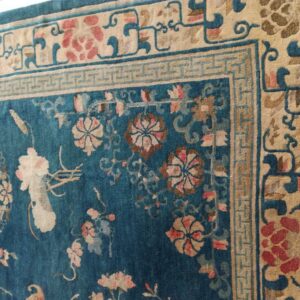 Teal rug corner featuring intricate tan, pink, and blue floral motifs with a detailed Greek key border.