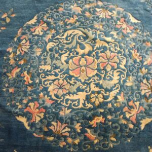 Deep blue rug with a carved pile displaying a detailed floral medallion in pink, gold, and light blue.