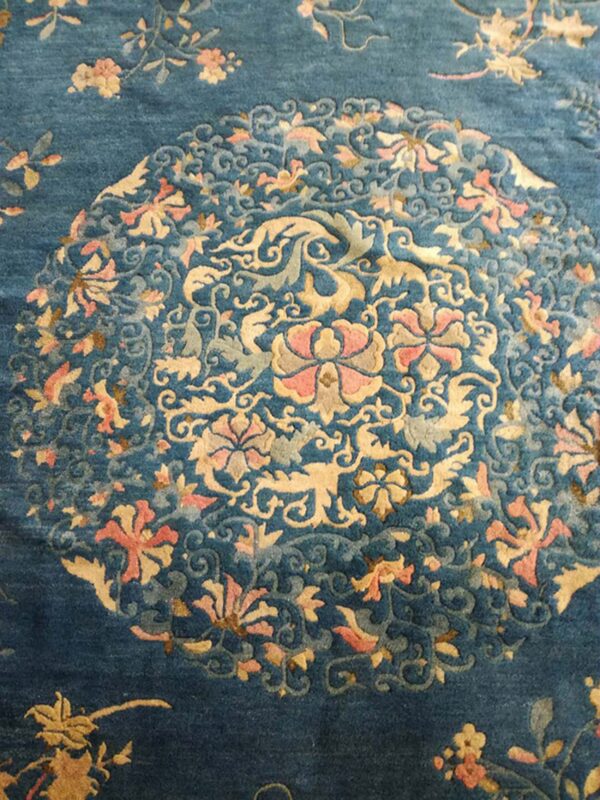 Deep blue rug with a carved pile displaying a detailed floral medallion in pink, gold, and light blue.