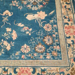 Teal rug with subtle sheen, featuring ornate pink and cream floral motifs and a structured beige border.