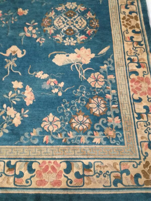 Teal rug with subtle sheen, featuring ornate pink and cream floral motifs and a structured beige border.