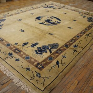 Large tan rug with blue landscape motifs, birds, and decorative borders on a distressed wood floor.
