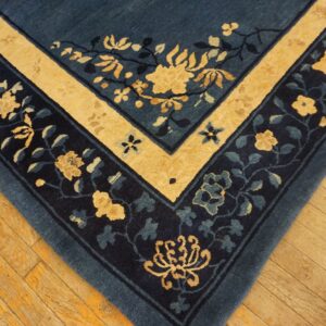 A corner of a dark blue rug with yellow and navy floral borders rests on light brown wood flooring.