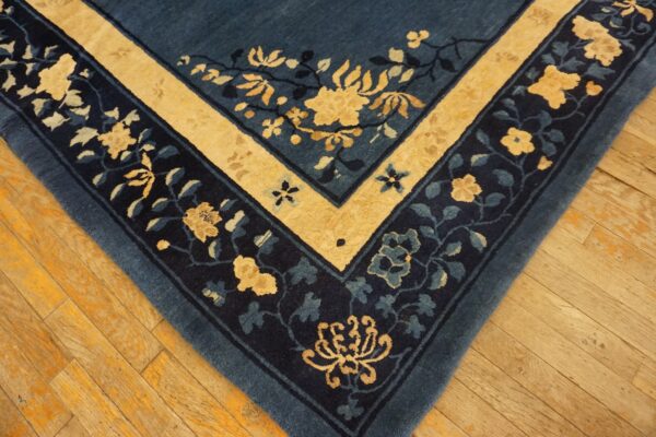 A corner of a dark blue rug with yellow and navy floral borders rests on light brown wood flooring.