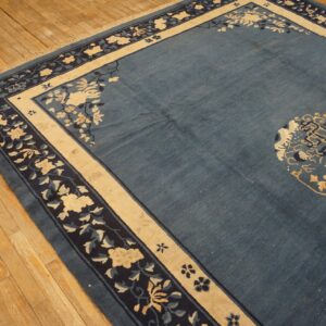 Low-pile blue rug with contrasting cream and navy floral borders shown on light wood planks.