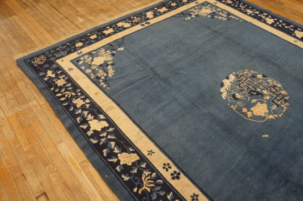 Low-pile blue rug with contrasting cream and navy floral borders shown on light wood planks.