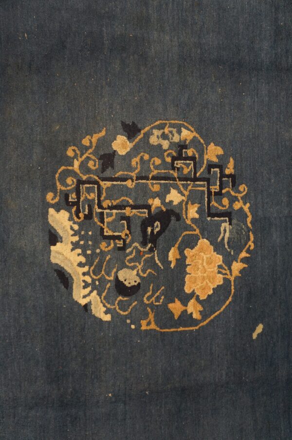 Detail of a deep blue rug showing a circular design featuring golden floral elements and dark fretwork.