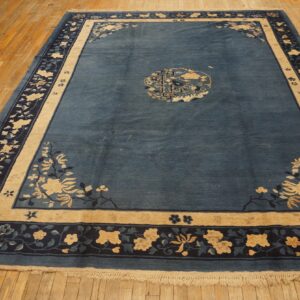A dark blue rug featuring beige and navy floral patterns rests on distressed natural wood flooring.