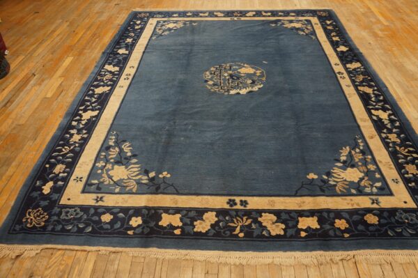 A dark blue rug featuring beige and navy floral patterns rests on distressed natural wood flooring.
