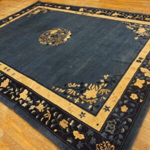 Low-pile slate blue rug featuring beige and dark navy floral borders rests on rustic wood flooring.