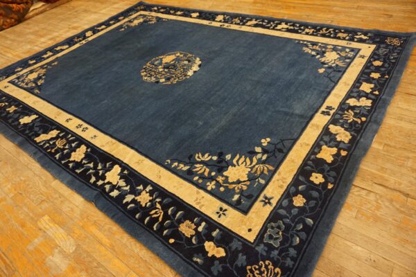 Low-pile slate blue rug featuring beige and dark navy floral borders rests on rustic wood flooring.