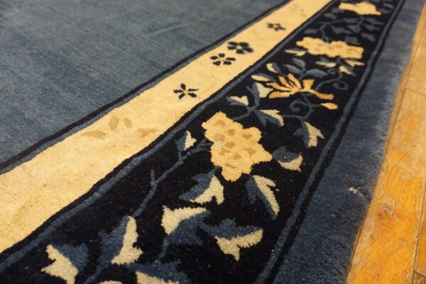 A navy and pale yellow floral border edges a denim blue high-pile rug lying on wood plank flooring.