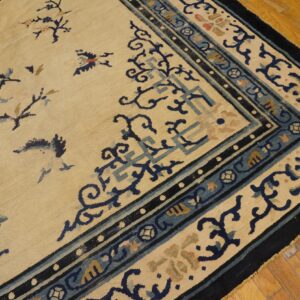 Close-up of a beige rug featuring ornate dark blue and dusty blue borders on wood flooring.