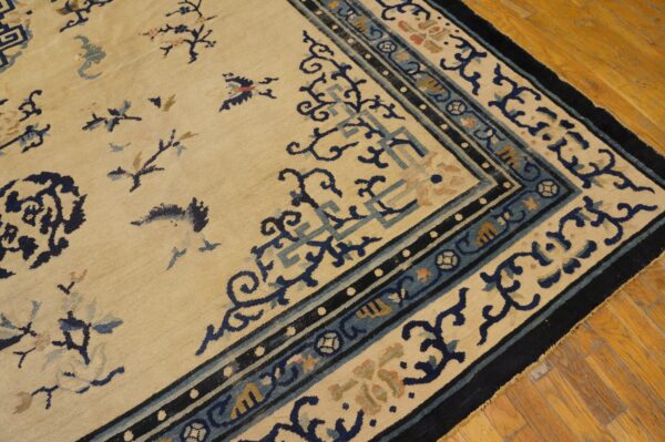 Close-up of a beige rug featuring ornate dark blue and dusty blue borders on wood flooring.