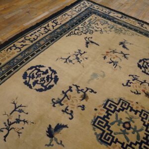 Tan rug featuring a low pile, deep blue borders, and scattered botanical and bird motifs on wood flooring.