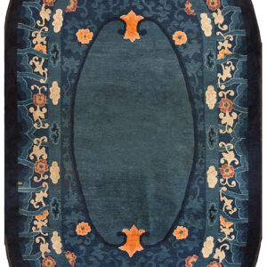 A detailed oval rug in deep blue features a central field bordered by ornate orange florals and beige scrollwork.