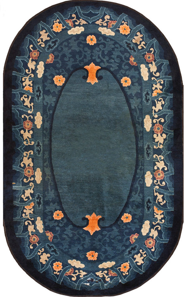 A detailed oval rug in deep blue features a central field bordered by ornate orange florals and beige scrollwork.
