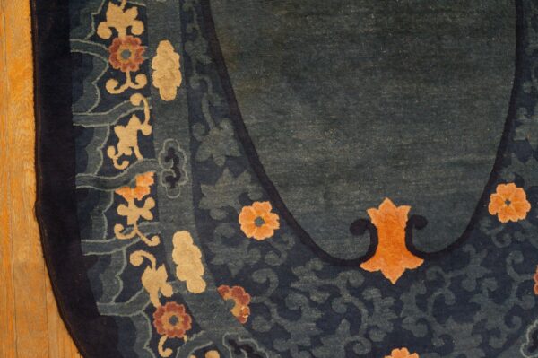 Teal and navy rug border featuring stylized tan and orange flowers rests beside light golden hardwood floorboards.