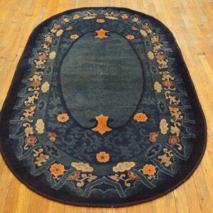 Oval dark blue rug with a central teal field and a multicolored floral border on wood floor.