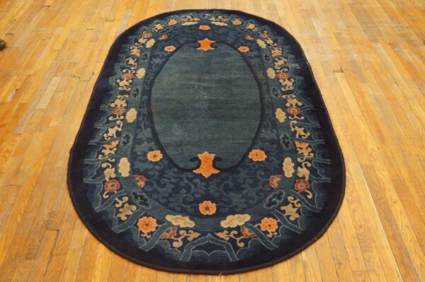 Oval dark blue rug with a central teal field and a multicolored floral border on wood floor.