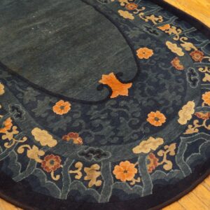 Oval blue rug with stylized gold and orange floral pattern bordering a dark teal center on wood planks.