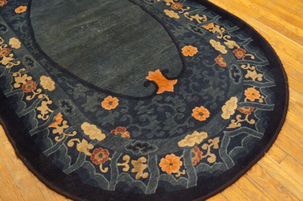 Oval blue rug with stylized gold and orange floral pattern bordering a dark teal center on wood planks.