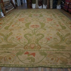 Large tan rug with a formal green and coral scrolling floral pattern on a wood floor.