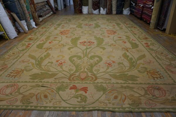 Large tan rug with a formal green and coral scrolling floral pattern on a wood floor.