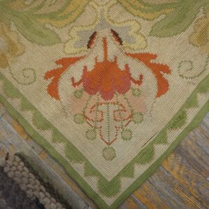 Low-pile beige rug with orange and green floral border design rests on weathered wood planks.