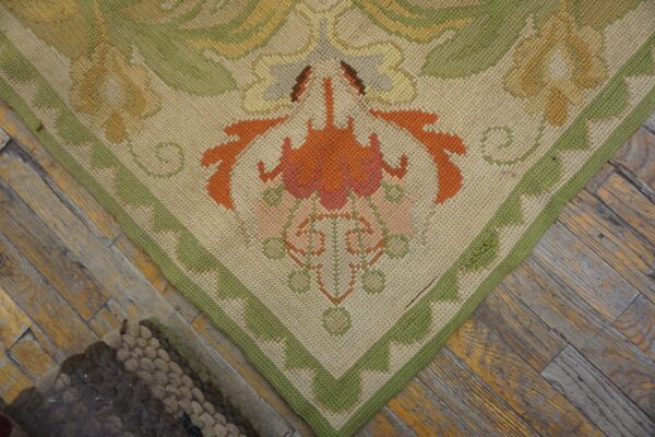 Low-pile beige rug with orange and green floral border design rests on weathered wood planks.