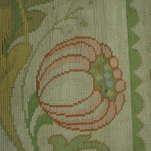 A tight woven low-pile rug shows a peach and rust flower with pale green leaves on a cream background.