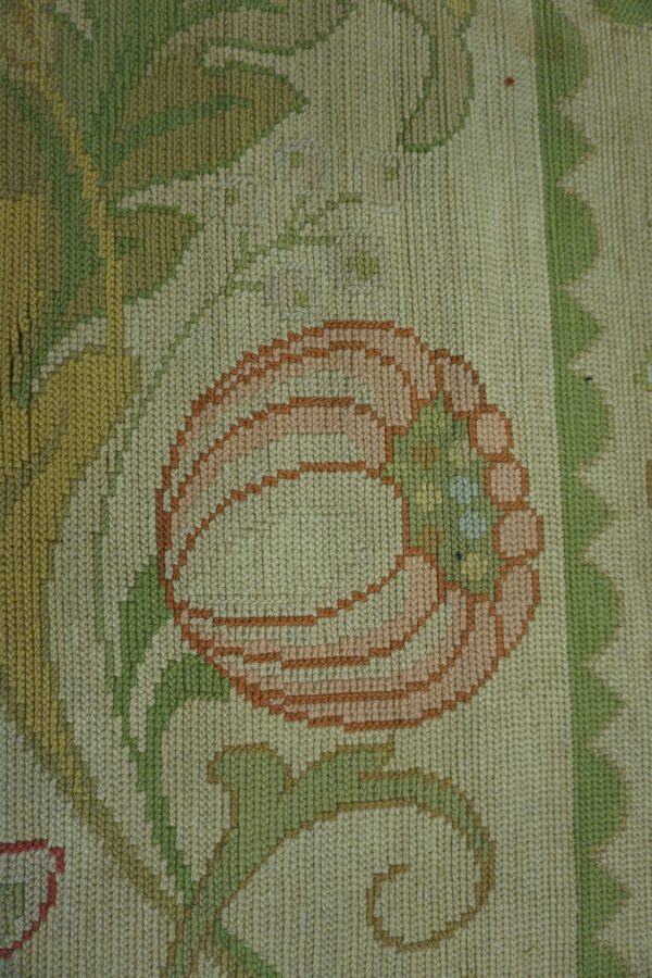 A tight woven low-pile rug shows a peach and rust flower with pale green leaves on a cream background.
