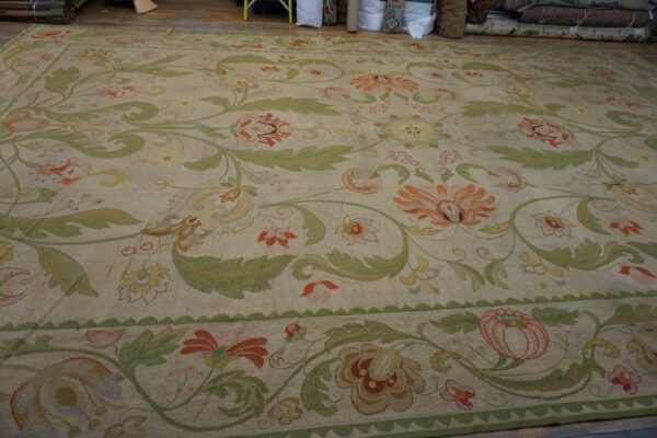 Beige rug with large green leaves and colorful florals laid on a wood floor near stacked rolls.