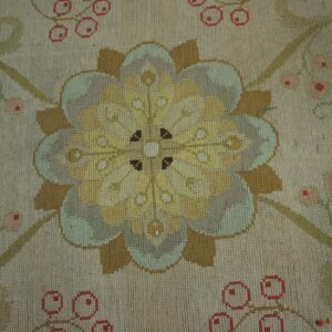 Muted floral rug detail showing a stylized yellow medallion, tan leaves, and pink berries on a beige ground.