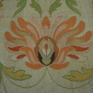 A close-up shows a cream rug with a large orange, peach, and green stylized floral needlepoint design.