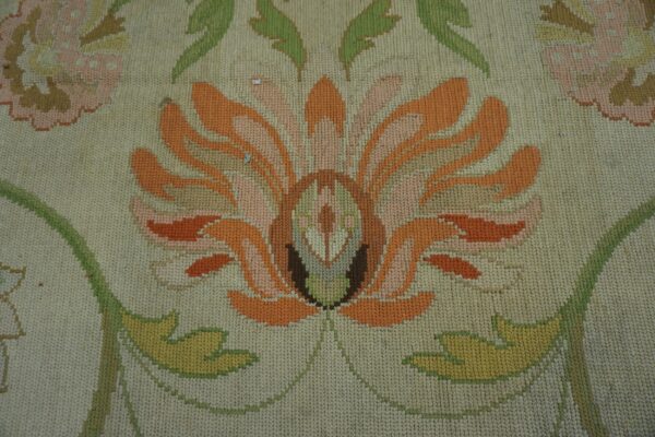 A close-up shows a cream rug with a large orange, peach, and green stylized floral needlepoint design.